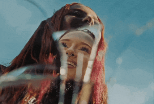 a woman with red hair and a nose ring looks at her reflection in a mirror