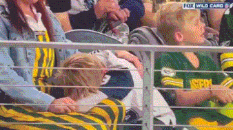 a boy in a green bay packers jersey is sitting in a stadium with a woman .