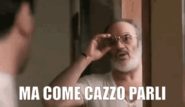 a man with glasses is looking at himself in a mirror and says ma come cazzo parli