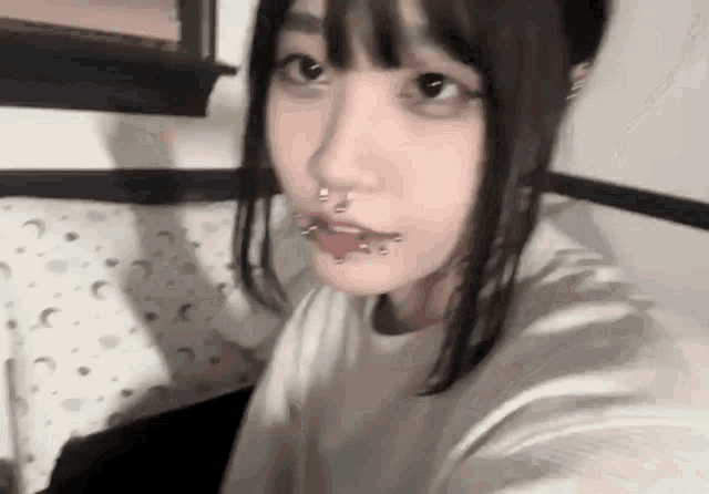 a young girl with piercings in her nose and mouth is taking a selfie .