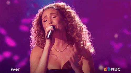 a woman singing into a microphone with the nbc logo in the corner