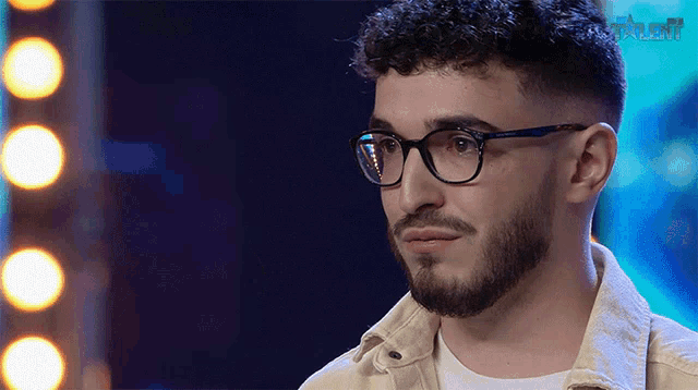 a man with glasses and a beard looks at the camera with talent written on the bottom