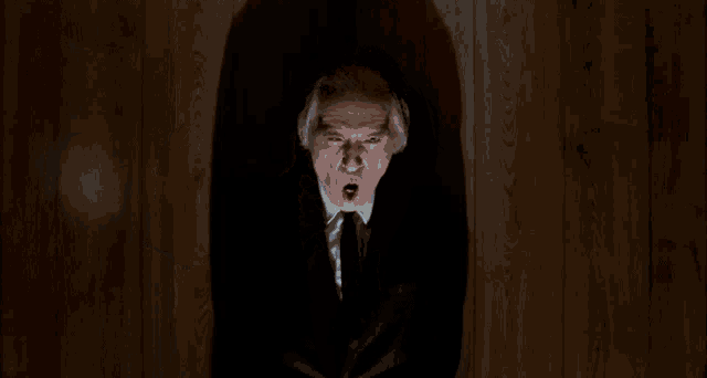 a man in a suit and tie is laying on a wooden floor looking up at the camera .