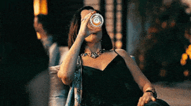 a woman in a black dress is sitting on a couch drinking a glass of beer .