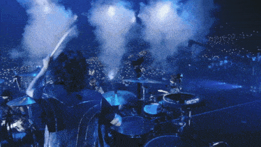 a man playing drums in front of a crowd with smoke coming out of the drum set