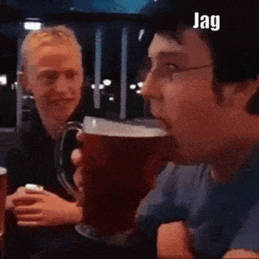 a man is drinking a beer from a mug while a woman watches .