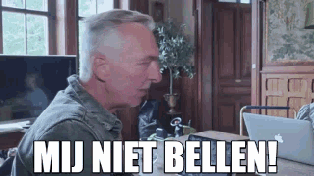 a man is sitting at a table with a laptop and a sign that says mij niet bellen !
