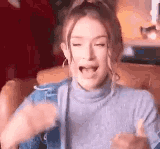 a woman in a blue sweater is sitting in a chair with her mouth open .