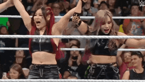 a couple of women are standing in a wrestling ring with their hands in the air .