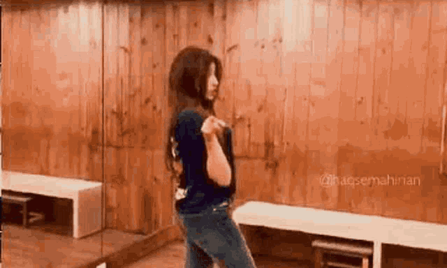 a woman is dancing in front of a mirror in a room with wooden walls .