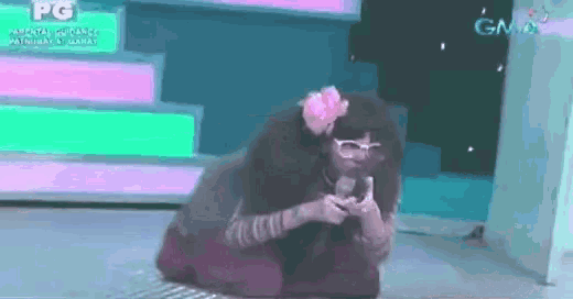 a woman with glasses and a flower in her hair is kneeling down in front of a gma sign