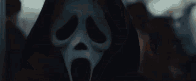 a close up of a scream mask with a black hood on .