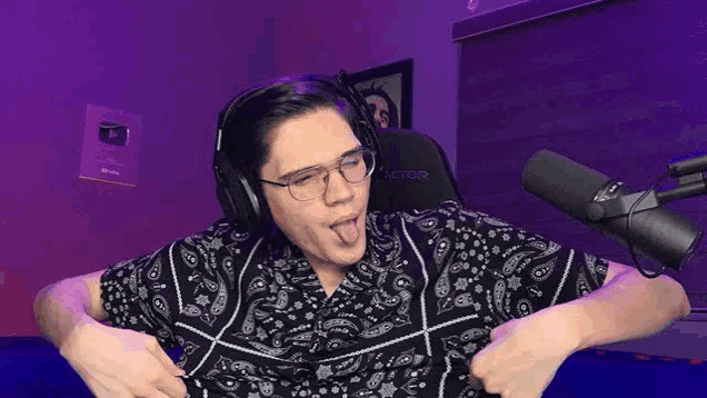 a man wearing headphones and glasses is sticking his tongue out while sitting in front of a microphone .