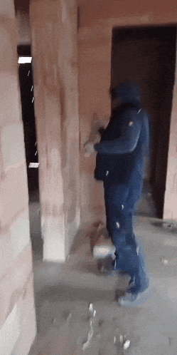 a man in blue overalls is standing in a room with brick walls