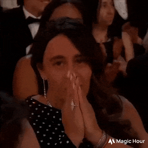 a woman in a black dress is sitting in a crowd with her hands on her face .