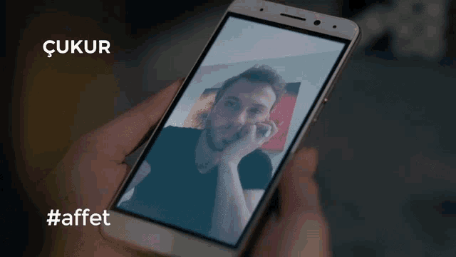 a close up of a woman looking at a cell phone with the words çukur #affett visible