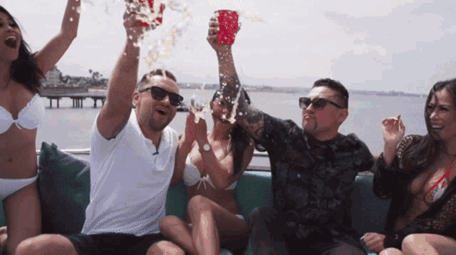 a group of people sitting on a couch with a man holding a red cup in the air