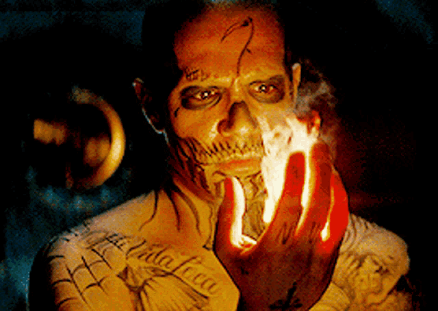 a man with a skull painted on his face has a tattoo on his arm that says " la vida loca "
