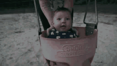 a baby is sitting in a pink swing being held by a person .