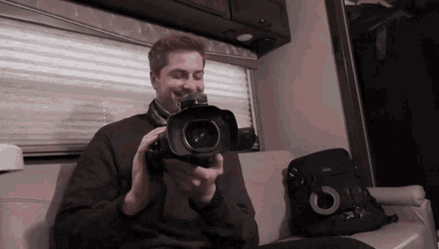 a man in a brown sweater is holding a camera in his hands