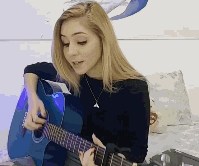 a woman playing a blue guitar with a whale tail necklace