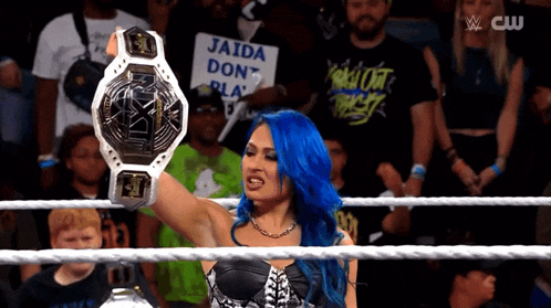 a woman with blue hair is holding up a wrestling championship belt