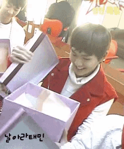 a boy in a red vest is opening a purple box and smiling
