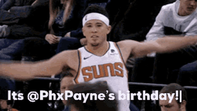 a basketball player wearing a suns jersey is standing in the stands with his arms outstretched .