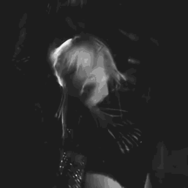 a black and white photo of a woman singing into a microphone while standing on a stage .