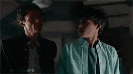 two young men are standing next to each other in a dark room and talking to each other .