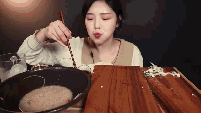 a woman eating food with chopsticks from a bowl on a wooden table