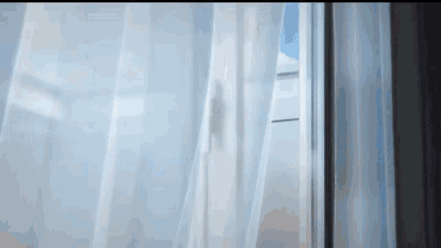 a window with white curtains open and a blue sky in the background