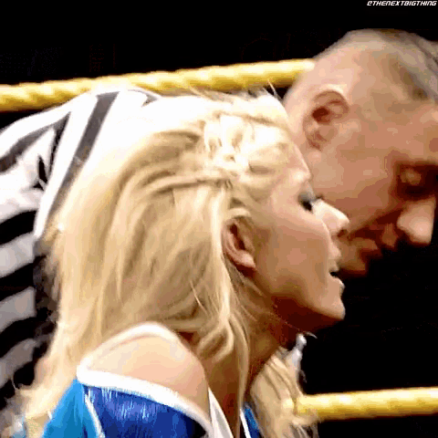 a woman in a blue and white outfit is talking to a referee in a wrestling ring