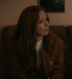 a woman with long red hair is sitting on a couch in front of a picture on the wall