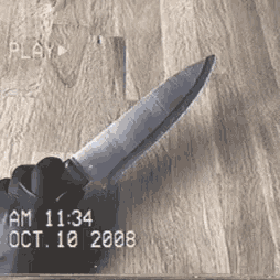 a hand is holding a knife on a wooden surface .