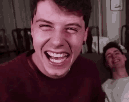 a man is making a funny face while sitting on a couch with another man .