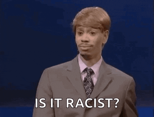 a man in a suit and tie is standing on a stage and asking is it racist .