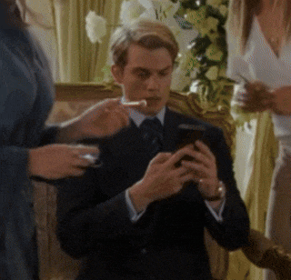 a man in a suit and tie is smoking a cigarette while looking at his phone