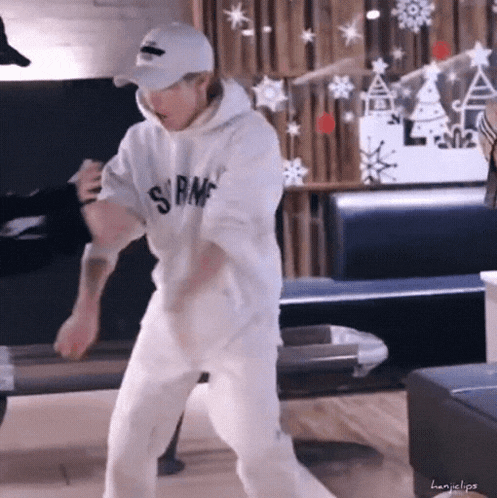 a man wearing a hoodie and a baseball cap is dancing in a living room .