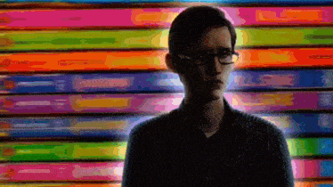 a man wearing glasses stands in front of a colorful background .