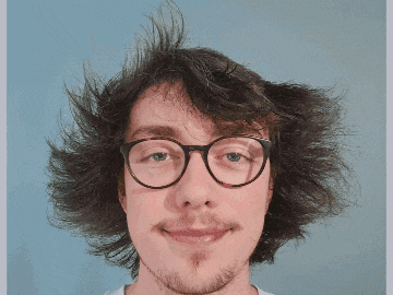 a man with glasses and a beard is smiling in front of a sign that says ' id ' on it