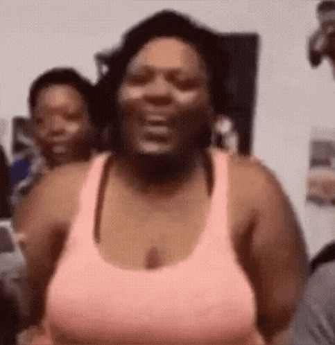 a woman in a pink tank top is laughing while standing in a room .