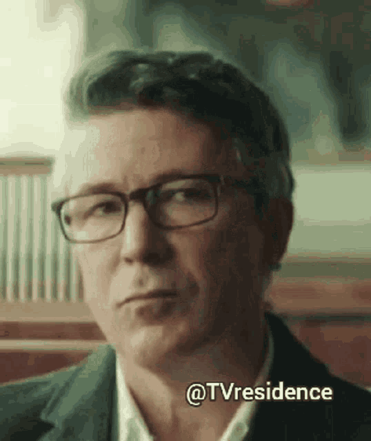 a man wearing glasses is sitting at a table with a caption that says tv residence