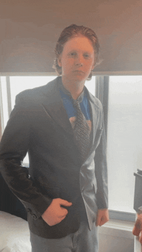 a young man wearing a suit jacket and tie stands in front of a window