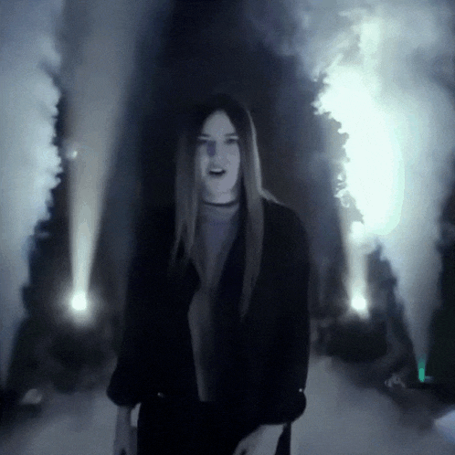 a woman in a black jacket is standing in front of a smoke machine