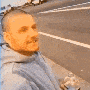 a man with a shaved head is taking a selfie on the side of the road