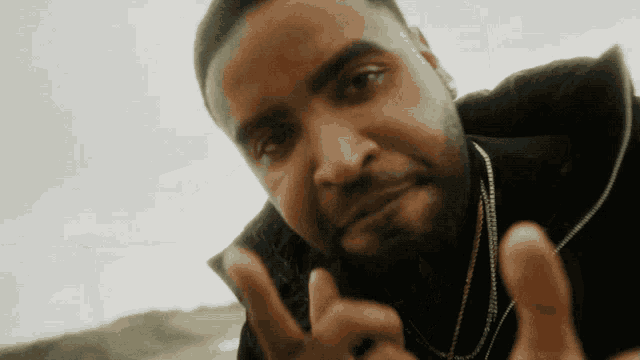 a man wearing a black jacket and gold chains is making a peace sign
