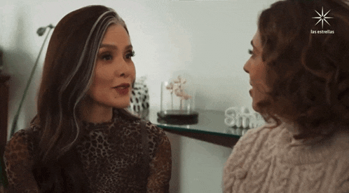 two women are talking in front of a sign that says " las estrellas "