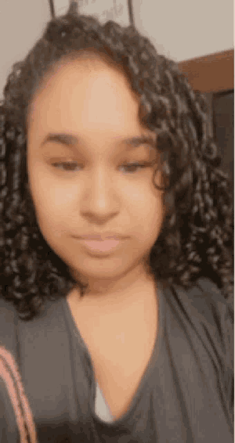 a woman with curly hair is wearing a black shirt and looking at the camera .