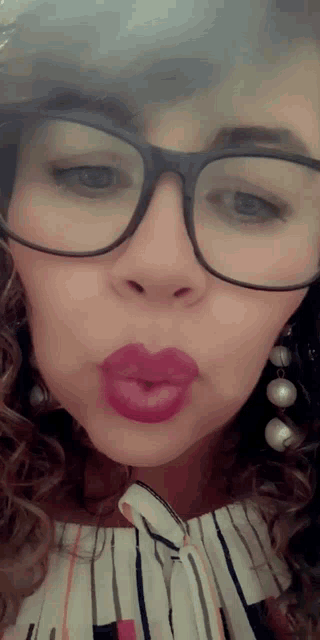 a woman wearing glasses and pearl earrings is blowing a kiss .